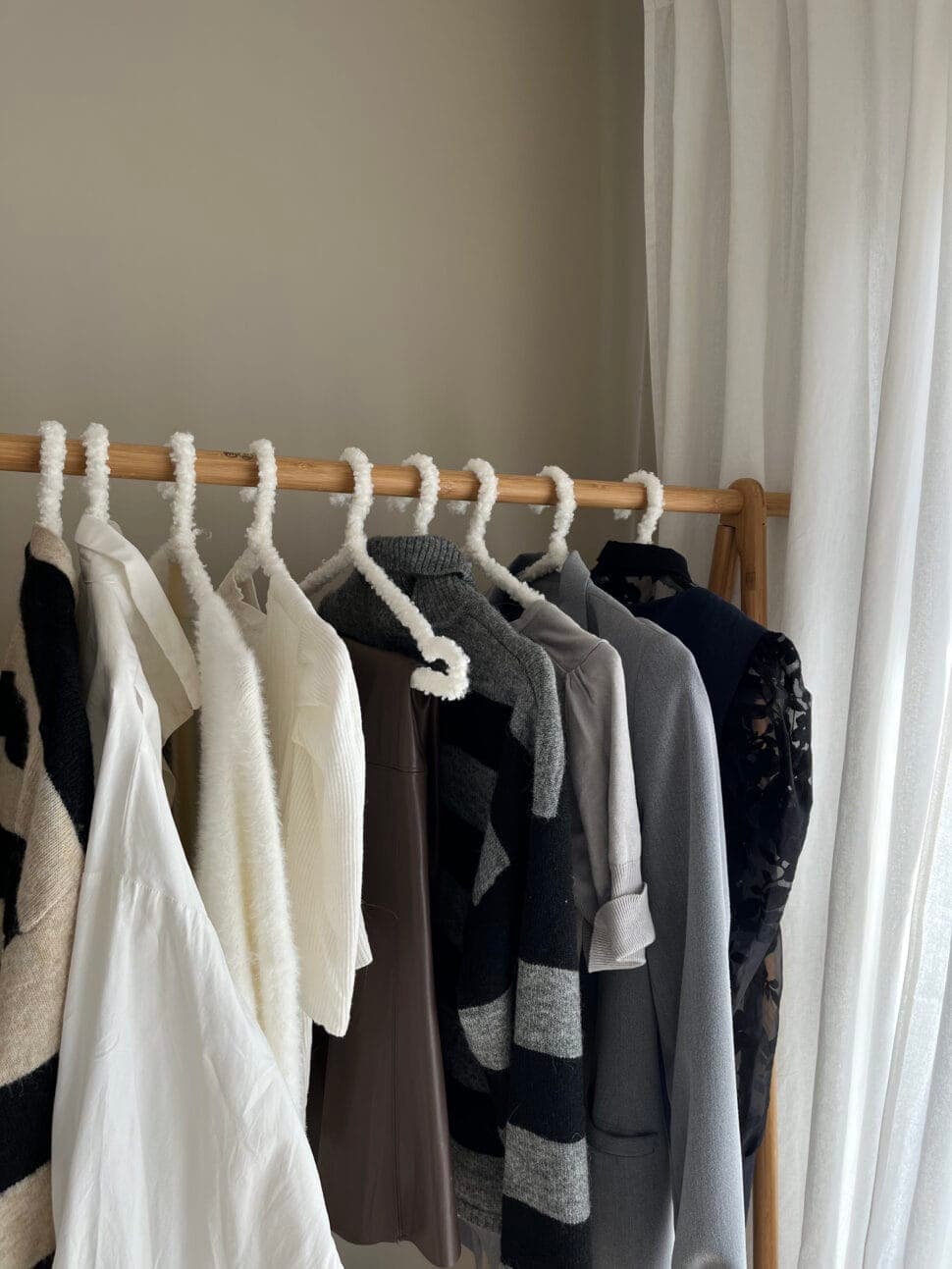 A wooden rail of winter knits and a dark floral dress, by a window