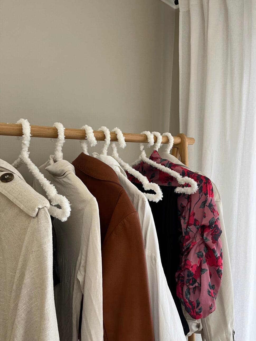 A beige coat, a brown shirt and a dark floral blouse on a rail