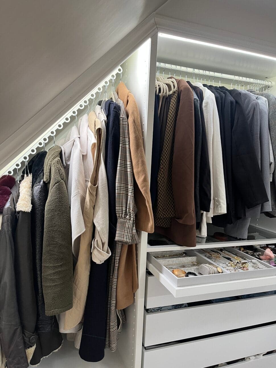 Coats and jackets on a lit rail in a walk-in wardrobe, drawers below